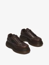 Zapato de cuero marrón con suela gruesa y redondeada, inspirado en modelos de los años 90. Presenta 5 ojales, pespuntes blancos y amarillos, cuello acolchado y cordones tonales.