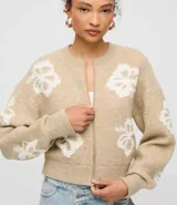 Cardigan cropped color beige con estampado de flores blancas, cuello redondo, cierre frontal con cremallera y mangas largas.