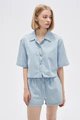 Camisa celeste de jean, corte cropped, con cuello camisero, cierre frontal con botones y mangas cortas.