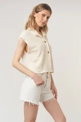 Camiseta negra con textura acanalada, corte holgado y cuadrado, cuello en punta, bolsillos amplios y botones funcionales.