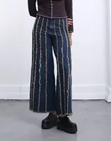 Pantalón jean de corte ancho con paneles verticales decorados con flecos.