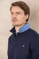 Chomba azul con cuello clásico, tapeta de dos botones y logo bordado en el pecho.