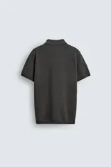 Jersey de punto color verde oliva, de calce relajado (relaxed fit), con cuello solapa y abertura frontal en forma de V. Es de manga corta y presenta acabados en rib en puños y ruedo.