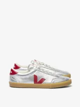 Zapatillas Veja modelo Volley, plateadas con logo lateral en rojo y contrafuerte en rojo. Suela de goma color caramelo y cordones blancos. Fabricadas con cuero orgánico y caucho amazónico.
