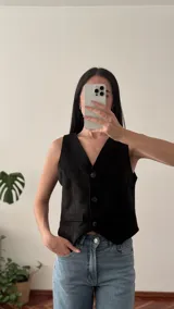 Chaleco sastrero negro de gamuza con cuello en V, cierre frontal con botones y bolsillos delanteros.