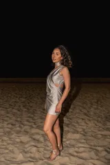 Vestido corto color plateado, con escote drapeado, sin mangas y corte en la cintura. Presenta abertura en la espalda y falda ajustada.