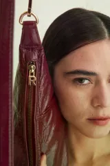 Bolso tipo baguette color borgoña de cuero brillante, con correa de hombro extraíble y herrajes dorados.