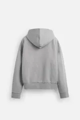 Sudadera gris con capucha, corte holgado, cierre frontal con cremallera, bolsillos laterales ocultos y terminaciones irregulares.