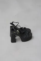 Sandalias negras de cuero sintético con plataforma y taco cuadrado. Tiras cruzadas sobre el empeine y pulsera con hebilla al tobillo.