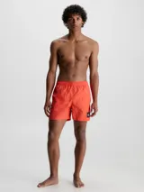 Short de baño rojo coral de largo medio, con cintura elástica y cordón ajustable. Incluye bolsillos laterales y trasero, forro de malla y logo de Calvin Klein en el lateral.