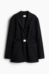 Blazer negro de botonadura simple con solapas de muesca, botones a presión ocultos adelante y cinturón extraíble con hebilla de metal. Modelo con hombreras, bolsillo insertado decorativo en el pecho y bolsillos delanteros ribeteados con solapa. Forrado.
