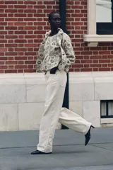 Blazer de tejido con estructura color crudo, con estampado de flores bordadas en negro. Tiene cuello solapa, manga larga y cierre frontal con botones negros.