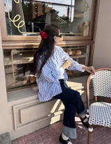Camisa celeste y blanca a rayas verticales, de corte amplio y mangas largas con puños anchos.