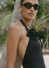 Traje de baño enterizo negro con escote halter y espalda descubierta. Presenta detalle de flor grande en el cuello.
