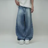 Jean de hombre, color celeste desgastado, corte ultra ancho (baggy) y tiro alto. Presenta un parche de cuero marrón con logo en el reverso de la cintura y un estampado circular blanco en el bolsillo trasero derecho.