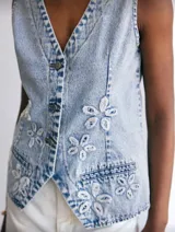 Chaleco de jean celeste con lavado ácido, con botones metálicos y apliques de flores blancas.
