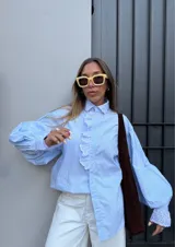 Camisa celeste a rayas verticales con cuello clásico y volados con bordado inglés en el frente y los puños.