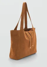 Bolso tipo shopper de gamuza color marrón, con doble asa corta y asa larga para el hombro. Tiene cierre de lazo y forro interior de algodón con un bolsillo con cremallera.