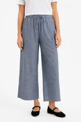 Pantalón de lino color beige, de corte ancho y tiro alto, con bolsillos laterales y cintura elastizada con cordón ajustable.