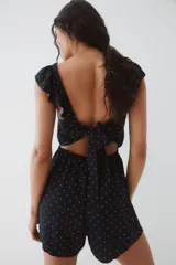 Mono corto negro con estampado de lunares blancos. Presenta escote cuadrado, breteles anchos con volados y elástico revestido en la cintura.