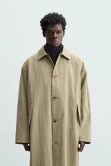 Gabardina color arena de corte amplio, con cuello solapa, manga larga, cierre frontal con botones y bolsillos laterales con solapa.