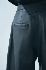 Pantalón de cuero negro de tiro medio, con pinzas delanteras, bolsillos laterales ocultos y corte holgado.