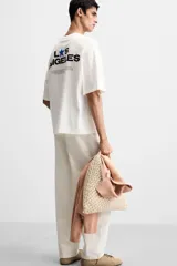 Camiseta blanca de corte holgado, cuello redondo y manga corta. Presenta un pequeño estampado de una estrella azul y un texto en negro en el frente.