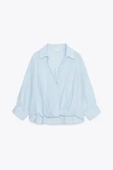 Camisa celeste de cuello solapa y manga 3/4 con puño. Tiene un nudo en el delantero y cierre frontal con botones.