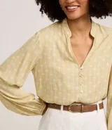 Camisa color amarillo pálido con estampado de palmeras blancas, cuello mao, cierre frontal con botones, mangas largas con puños elásticos y corte holgado.