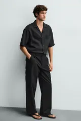 Pantalón negro de corte recto y calce relajado, confeccionado en tejido de algodón con elasticidad. Presenta cintura ajustable con cordón, bolsillos frontales y bolsillos traseros de doble vivo.