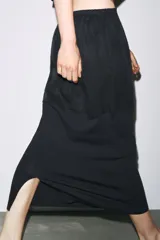 Falda midi negra de tiro alto con cintura elástica y frunces. Presenta detalle de tejido combinado y abertura en la parte trasera del ruedo.