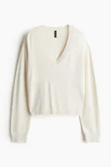 Sweater corto de punto fino color crema, con escote en V, hombros caídos y terminaciones acanaladas en puños y bajo.