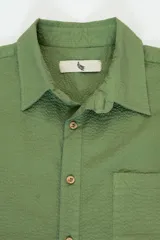 Camisa verde oliva de manga corta con textura seersucker, corte cuadrado, bolsillo en el pecho y botones de coco.