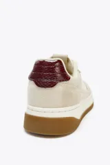 Zapatillas deportivas urbanas color beige y blanco, con detalles en color borgoña en el talón y laterales. Cierre con cordones y suela marrón de 3,5 cm de altura.