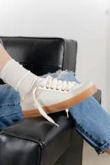 Zapatillas bajas color marfil con detalles dorados en el talón y ojales metálicos. Suela de goma color caramelo y cordones beige.
