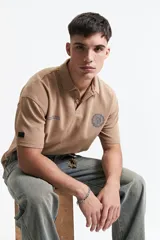 Remera polo color beige con textura acanalada, corte oversize, cuello clásico con botones y logo estampado en el pecho.