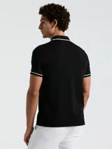 Chomba negra de piqué con cuello clásico, tapeta de dos botones y bolsillo de parche en el pecho con logo bordado. Detalles de ribete blanco en cuello y mangas.