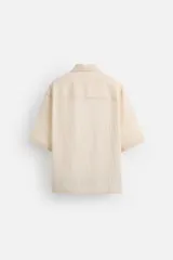 Camisa color crema de manga corta con cuello bowling, corte relaxed fit y bolsillo de parche en el pecho.