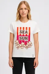 Remera blanca de algodón con estampado frontal de rayas rojas y texto "Sea Sun" con flores.