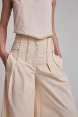 Pantalón negro de tiro alto, corte ancho y largo, con pliegues frontales y pespuntes contrastantes en blanco en la cintura y bolsillos.