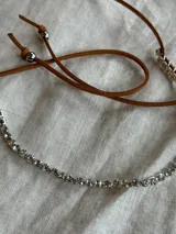 Gargantilla con tira de strass plateado y tiento de cuero marrón para atar.