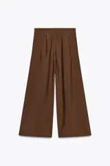 Pantalón cropped marrón de tiro medio y pierna ancha, confeccionado en hilatura con mezcla de lyocell. Presenta trabillas en la cintura, bolsillos laterales y pinzas en el delantero. Cierre frontal con cremallera y botón.