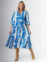 Vestido midi de corte amplio con estampado abstracto en tonos azules, blancos y beige. Tiene cuello en V, mangas 3/4 con volados y corte escalonado en la falda.