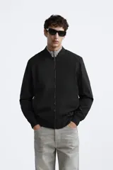Cazadora bomber ligera gris confeccionada en tejido técnico. Cuello y puños en rib elástico, manga larga, bolsillos de vivo en cadera y bolsillo interior. Cierre frontal con cremallera.