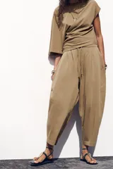 Pantalón color marrón claro, de tiro medio, corte ancho y largo tobillero. Cuenta con cintura elástica ajustable con cordones y bolsillos laterales ocultos en la costura.