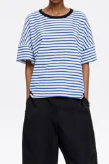 Camiseta de algodón a rayas horizontales azules y blancas, con cuello redondo negro, corte cuadrado y logo bordado en el pecho.