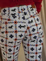 Pantalón de jean blanco con estampado de caballos negros, estrellas azules y motivos geométricos en naranja. Corte recto con aberturas en el ruedo.