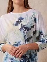 Buzo blanco estampado con flores azules y detalles en verde y amarillo, de la marca Milano. Tiene cuello redondo y mangas 3/4 con apliques de brillos en el frente.