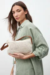 Bolso de hombro tejido a crochet color crema, con asas cortas de cuero marrón.
