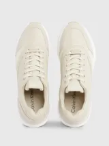 Zapatillas urbanas color beige, confeccionadas en cuero y tela, con suela blanca y cordones. Presentan monograma de la marca en el lateral.